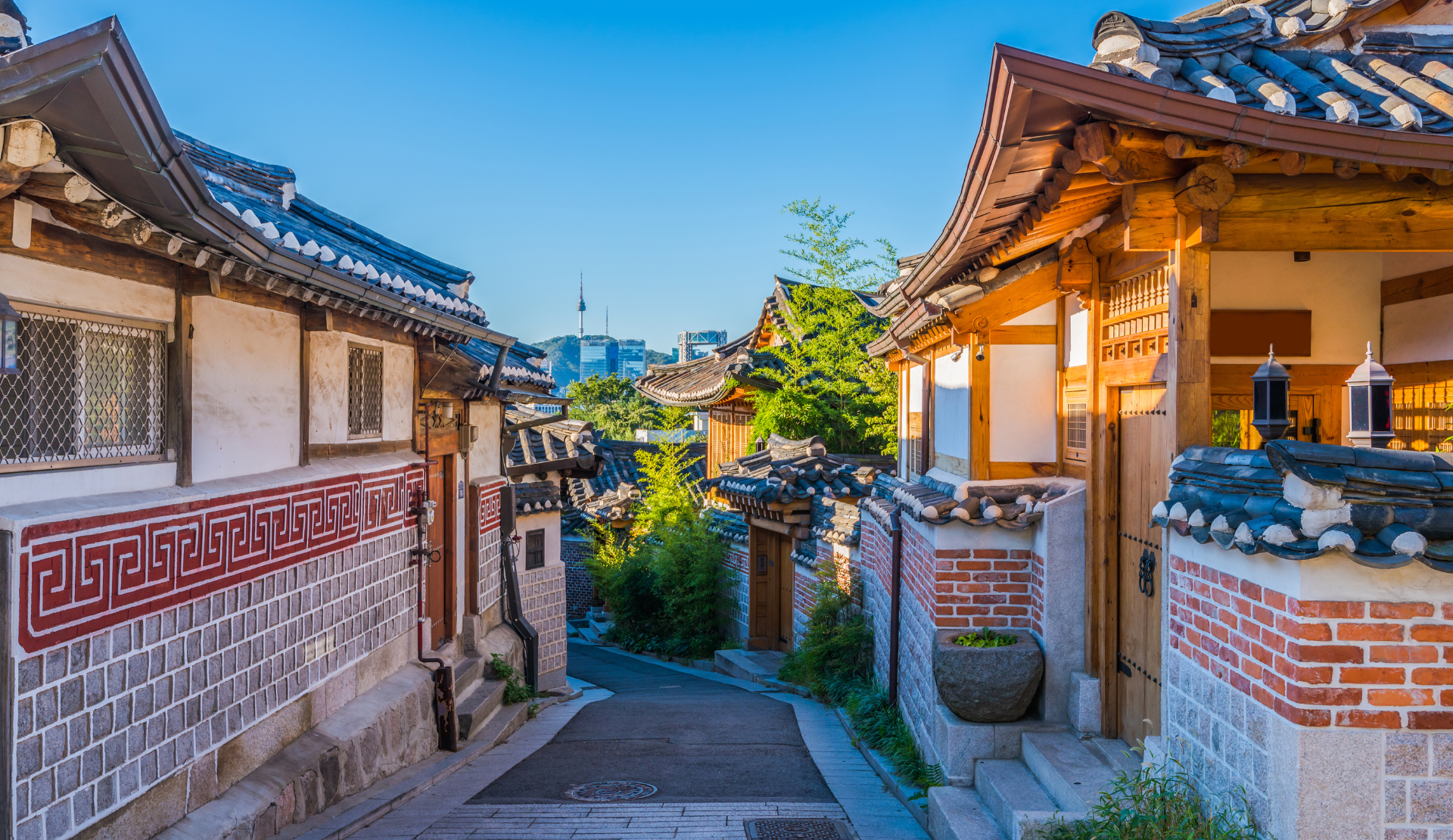 Blick in eine enge Gasse des Bukchon Hanok Village in Seoul mit traditionellen Hanok-Häusern auf beiden Seiten und dem N Seoul Tower im Hintergrund