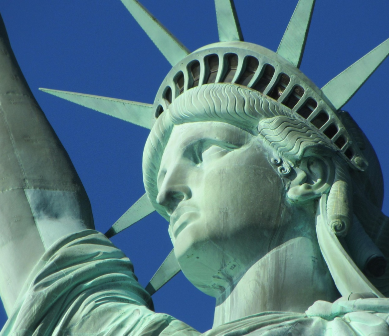 Detailaufnahme der Freiheitsstatue in New York mit erhobener Fackel vor blauem Himmel