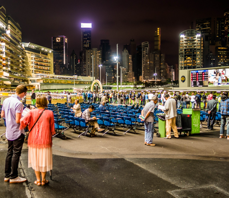 Paar beobachtet Vorbereitungen bei Happy Valley Racecourse in Hongkong mit aufgestellten Stühlen und beleuchteter Skyline bei Nacht