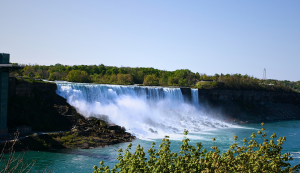 Blick auf die American Falls, einen der drei Wasserfälle der Niagarafälle, mit türkisfarbenem Wasser und Gischt unter blauem Himmel.