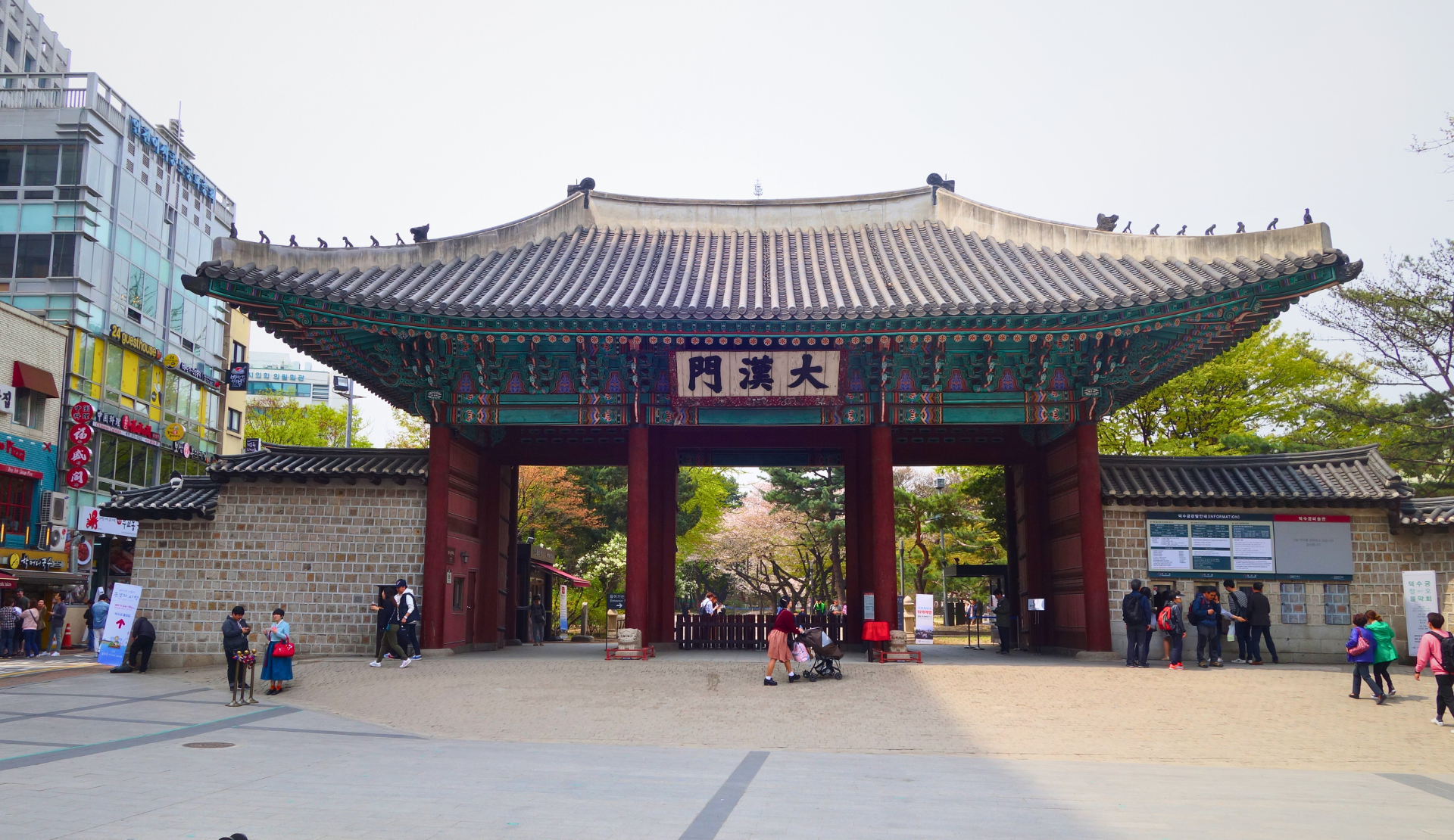 Das Haupttor Daehanmun des Deoksugung-Palastes in Seoul mit Besuchern und modernen Gebäuden im Hintergrund