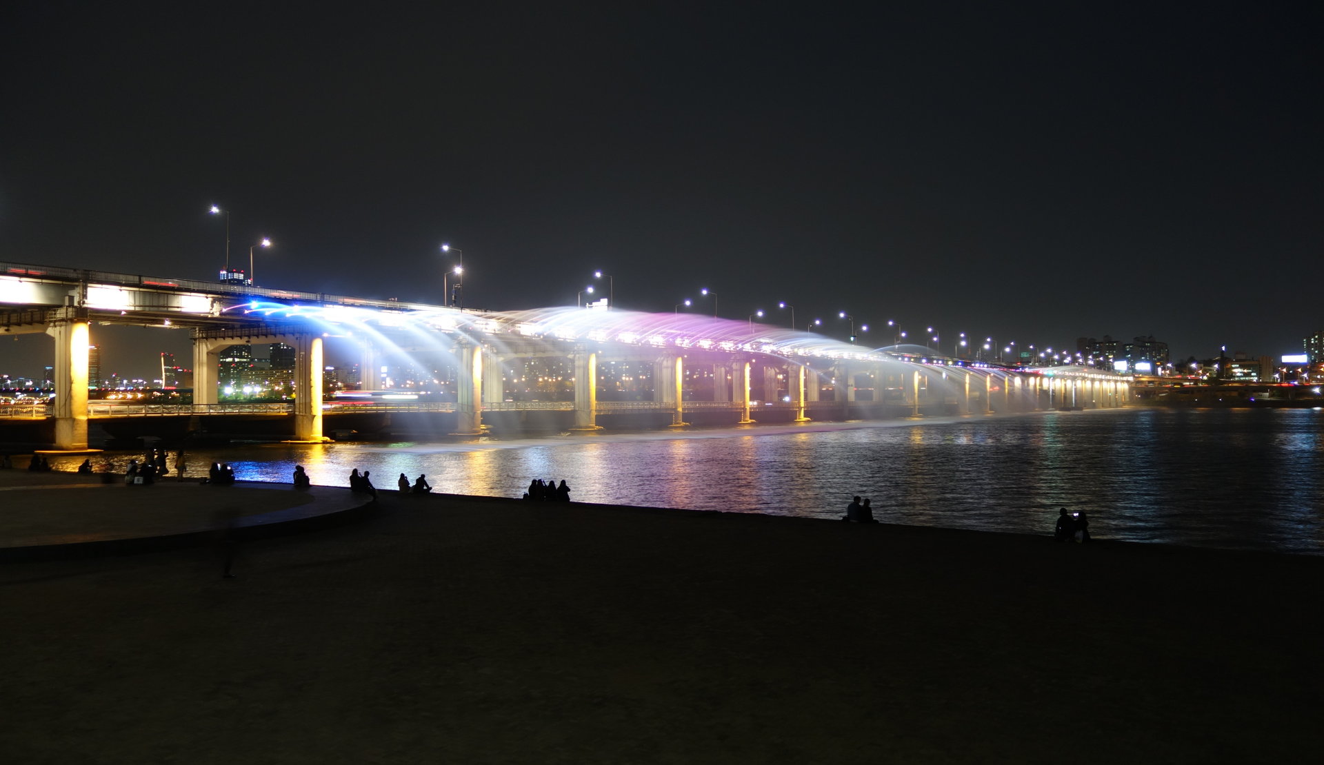 Die Banpo-Brücke in Seoul bei Nacht mit den beleuchteten Regenbogenfontänen, die das Wasser in den Han-Fluss sprühen