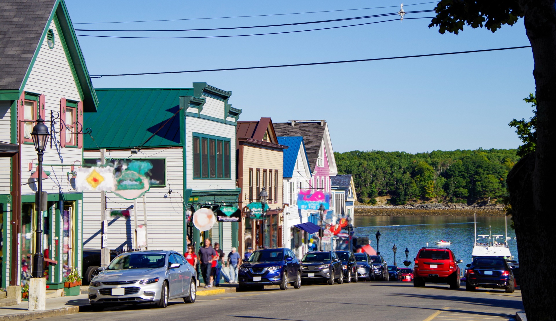 Main Street in Bar Harbor mit bunten Häusern, parkenden Autos und Blick auf den Hafen