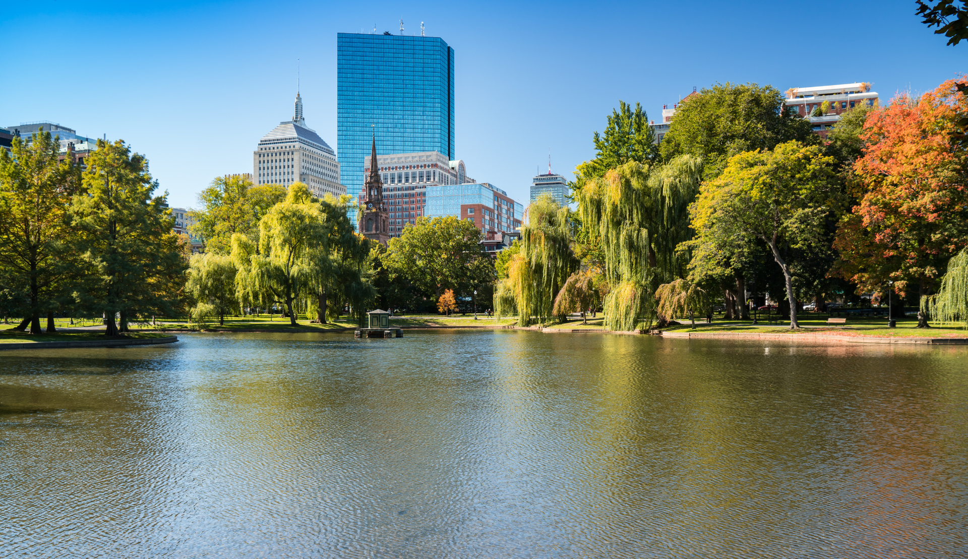 Blick über den Teich im Boston Public Garden mit Bäumen und moderner Skyline im Hintergrund