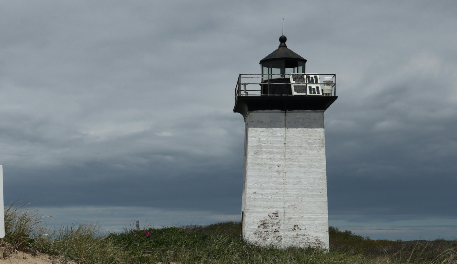 Weißer Leuchtturm an der Dünenküste von Cape Cod unter dunklem, bewölktem Himmel