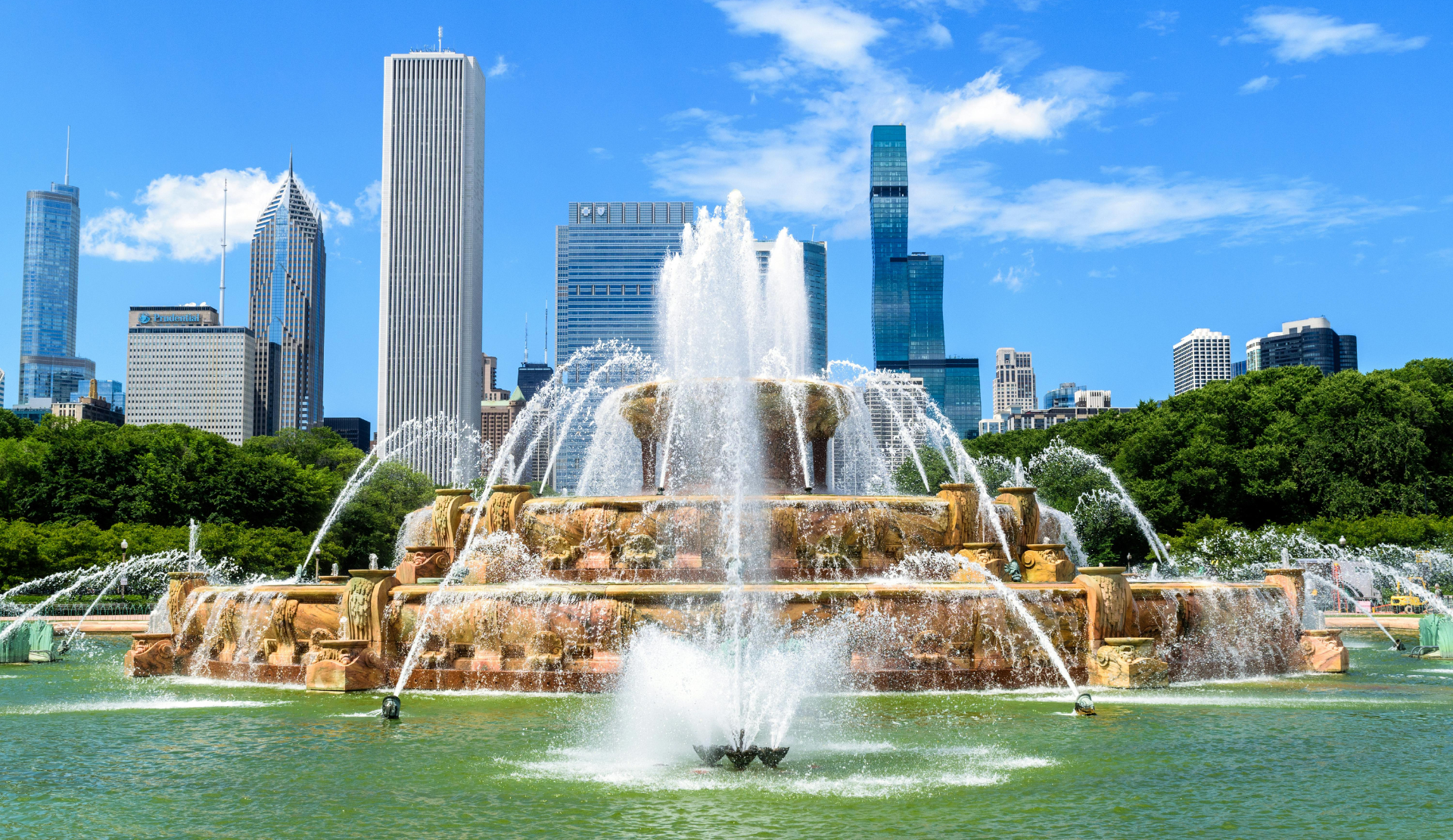 Der Buckingham Fountain im Grant Park Chicago mit Wasserfontäne und Skyline im Hintergrund an einem sonnigen Tag