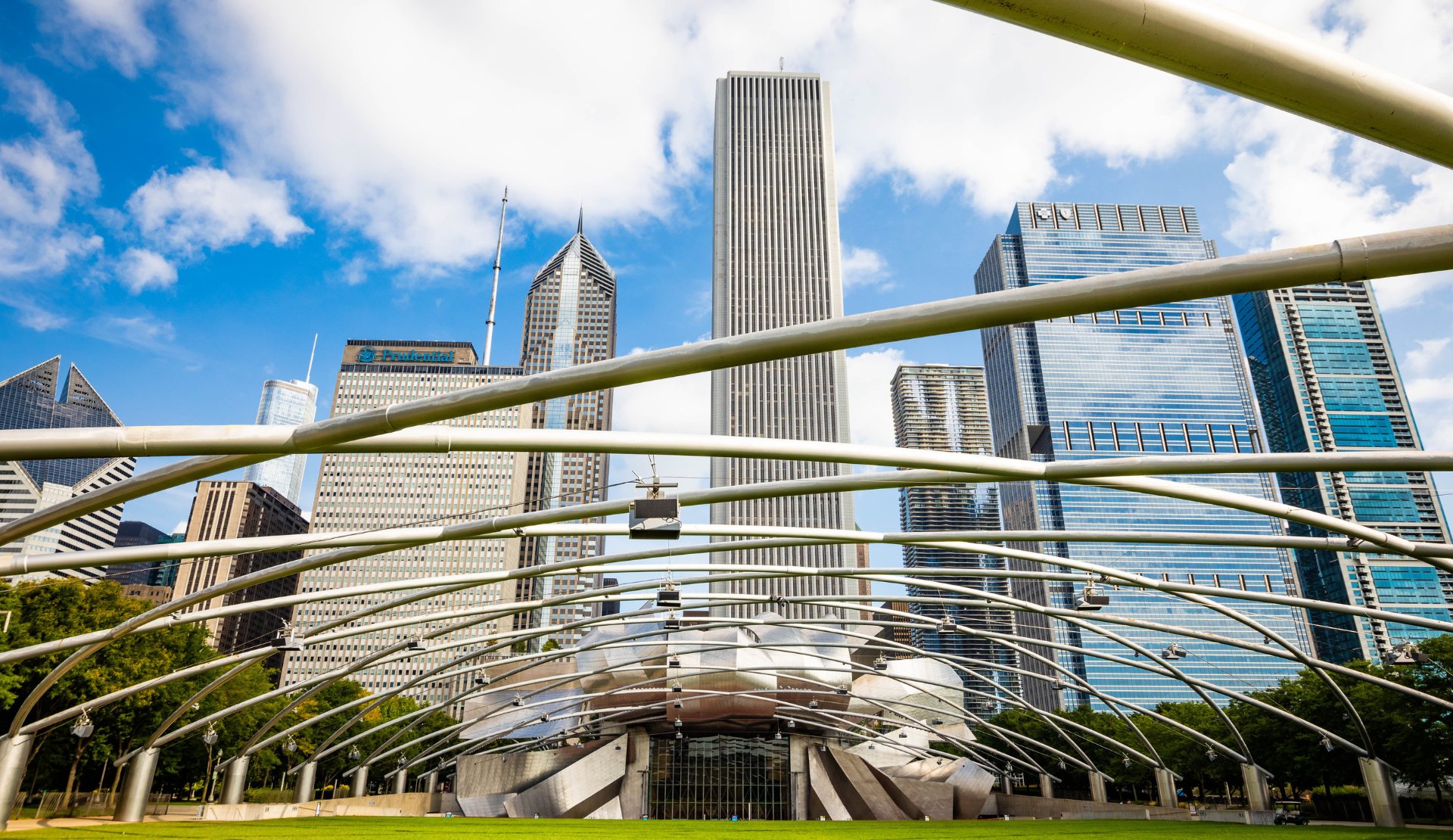 Blick auf den Millennium Park in Chicago mit grüner Rasenfläche, dem Jay Pritzker Pavilion und der Skyline im Hintergrund