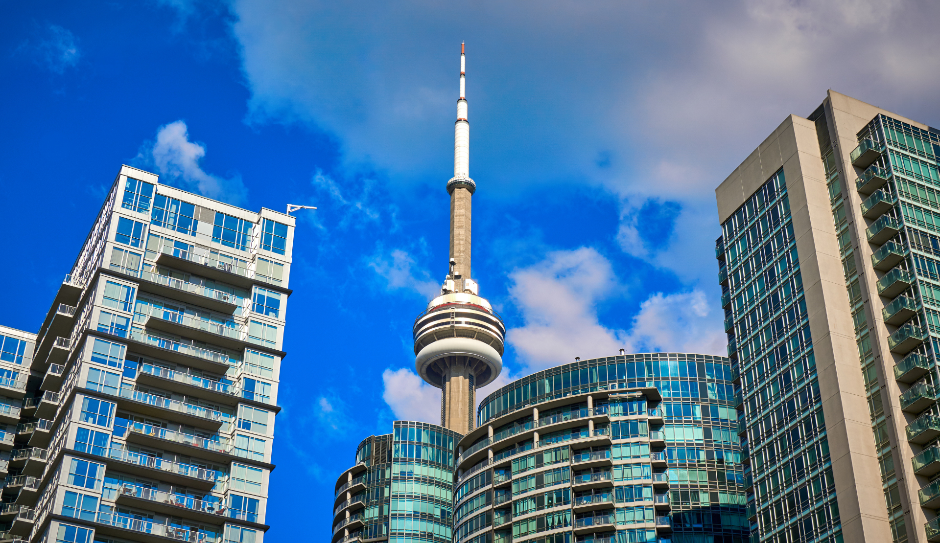 CN Tower in Toronto, fotografiert von unten zwischen modernen Hochhäusern bei blauem Himmel