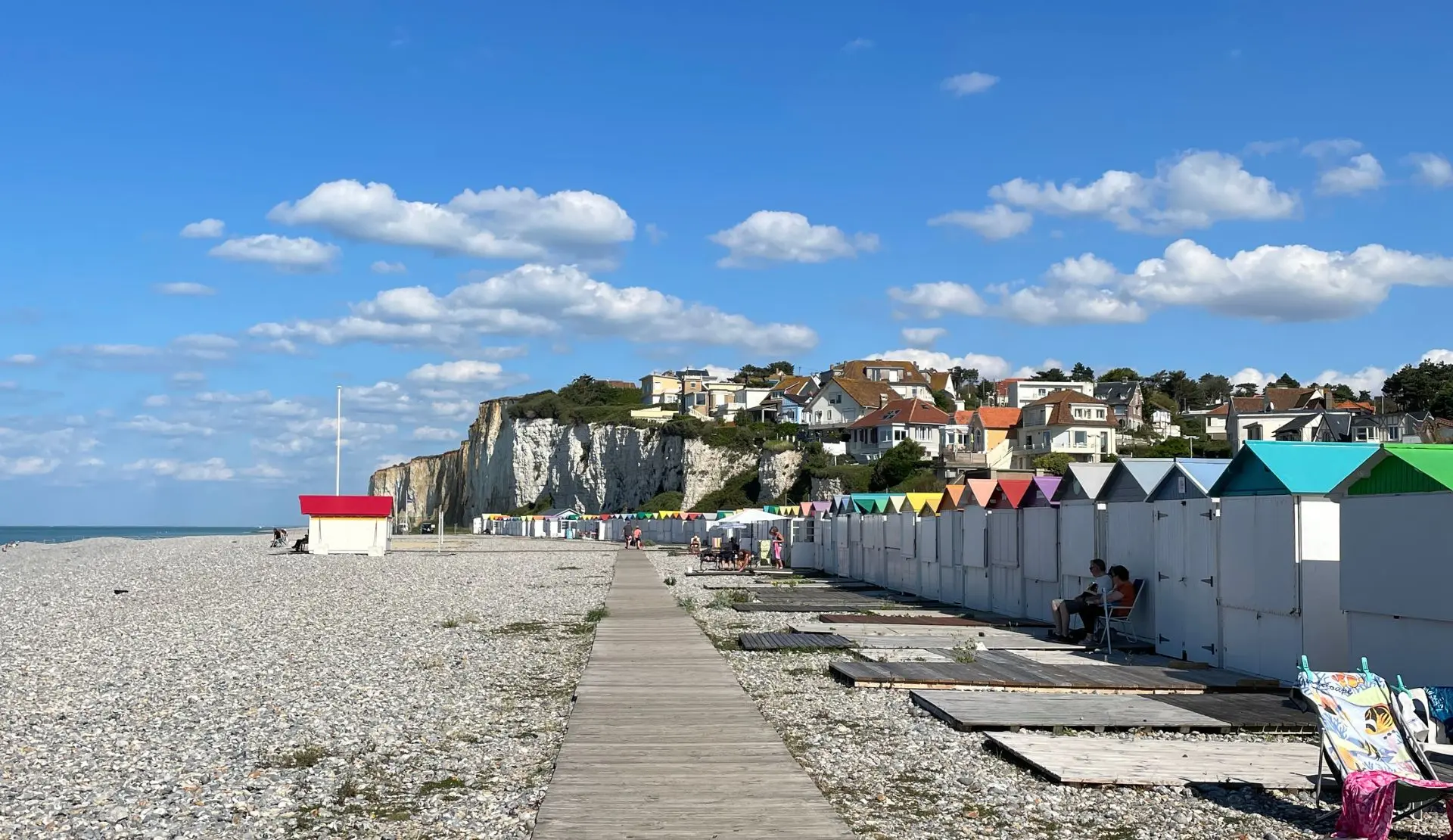 Kiesstrand mit bunten Strandhäuschen und Kreidefelsen in Criel-sur-Mer in der Normandie