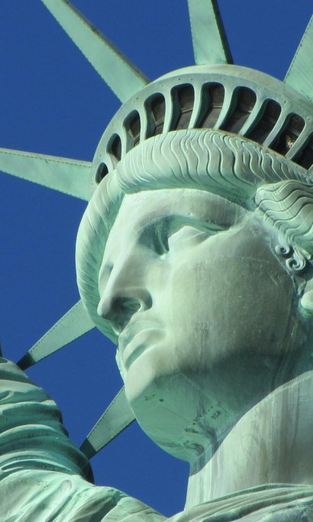 Detailaufnahme der Freiheitsstatue in New York mit erhobener Fackel vor blauem Himmel