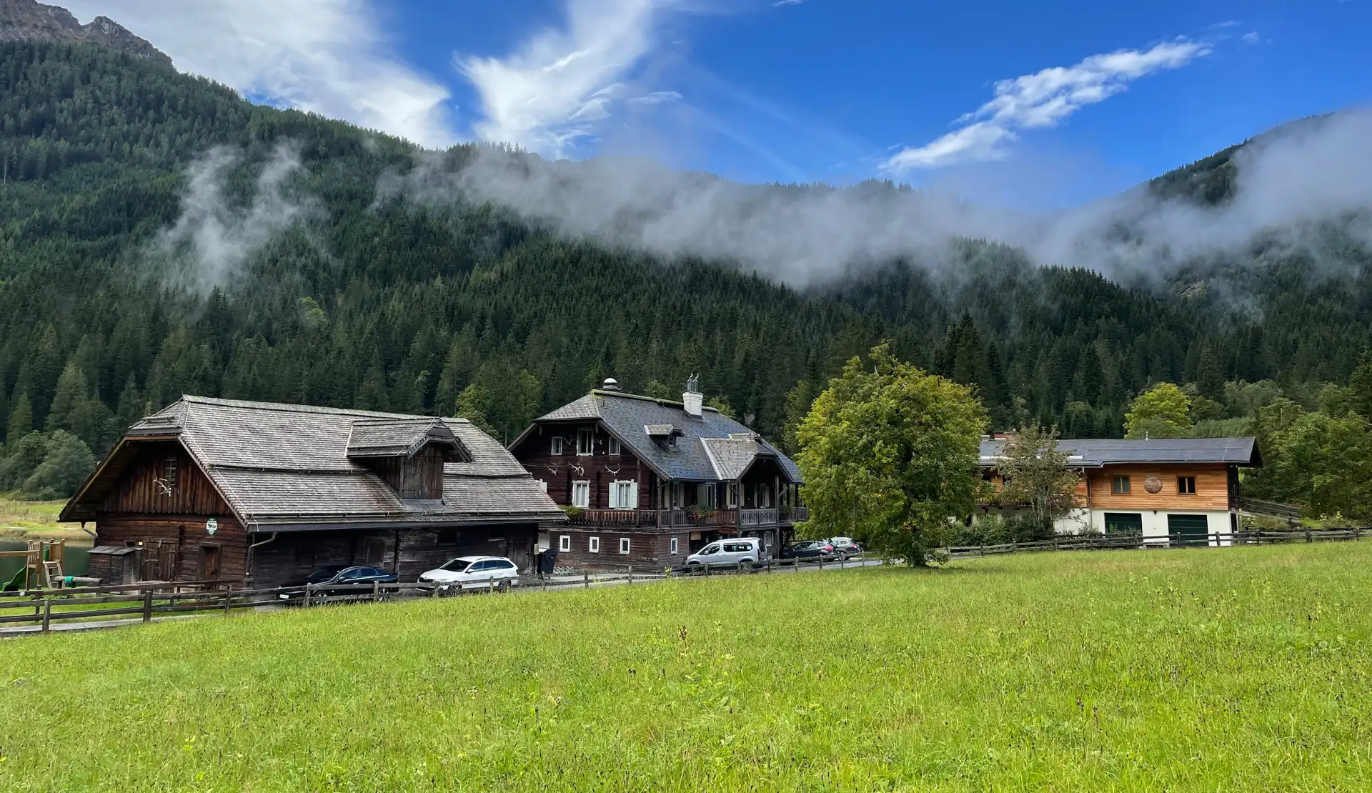 Gasthaus Jägersee in Kleinarl mit Holzhäusern auf einer Wiese und nebelverhangenen Wäldern im Hintergrund