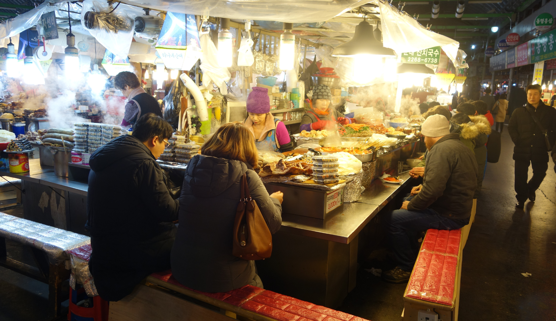 Belebte Foodstände im Gwangjang Market in Seoul mit dampfenden Speisen und Besuchern an den Tresen