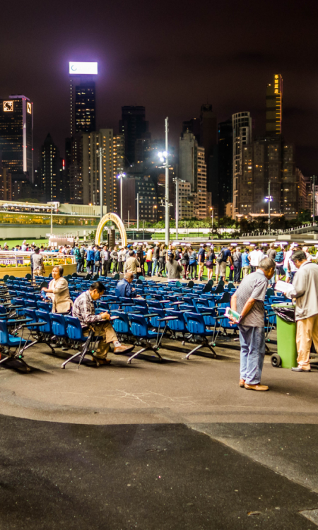 Paar beobachtet Vorbereitungen bei Happy Valley Racecourse in Hongkong mit aufgestellten Stühlen und beleuchteter Skyline bei Nacht