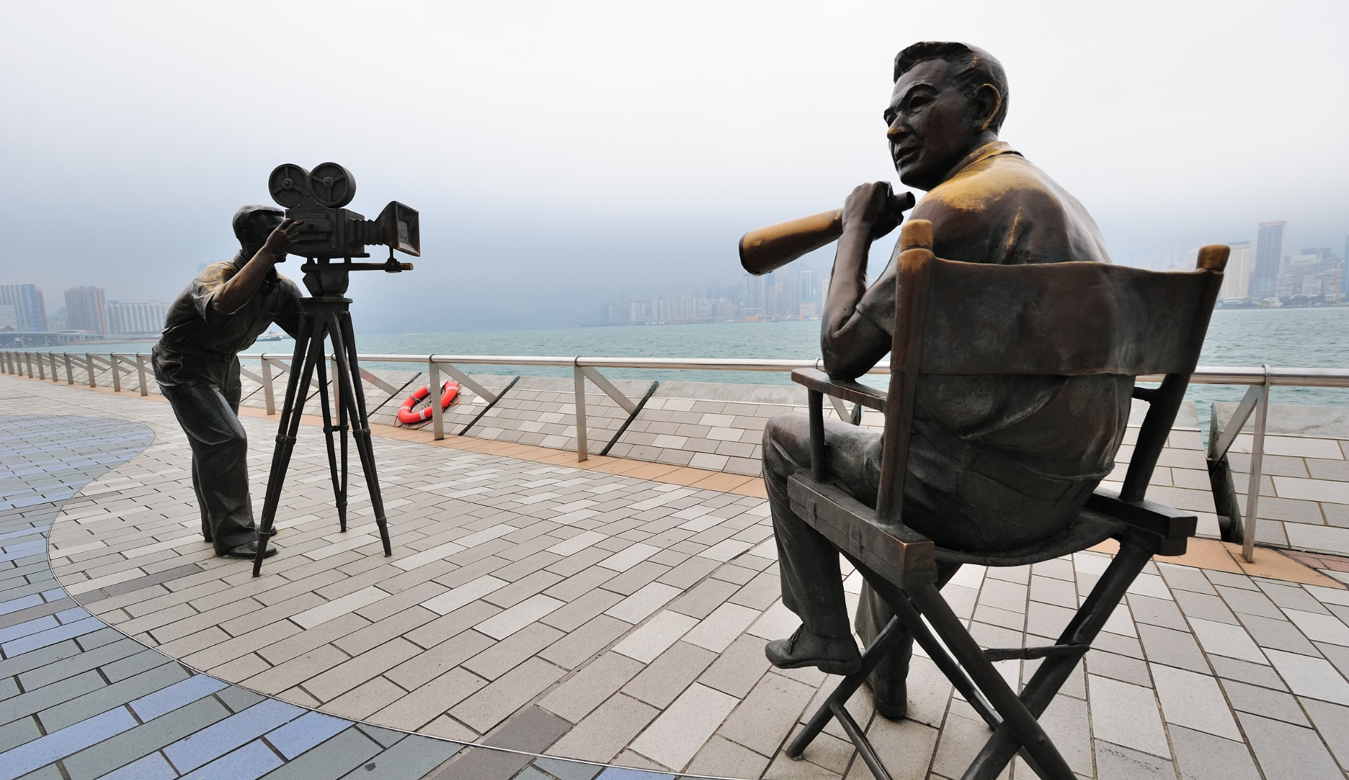 Bronze-Statuen an der Avenue of Stars in Hongkong zeigen Filmregisseur und Schauspieler mit Victoria Harbour Skyline im Hintergrund