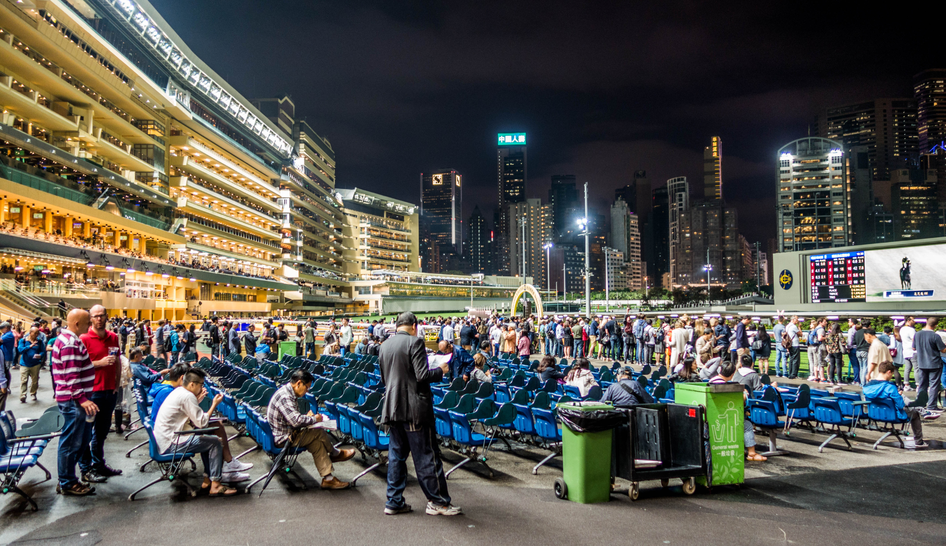 Happy Valley Racecourse in Hongkong bei Nacht mit vollbesetzten Tribünen, beleuchteter Rennbahn und imposanter Skyline im Hintergrund