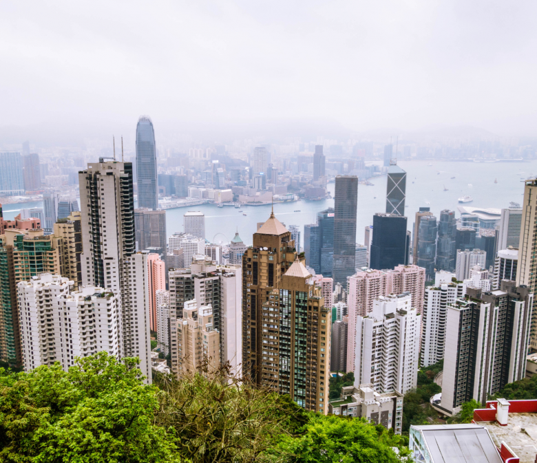 Hongkong Skyline vom Victoria Peak mit Wolkenkratzern, Victoria Harbour und grüner Vegetation im Vordergrund