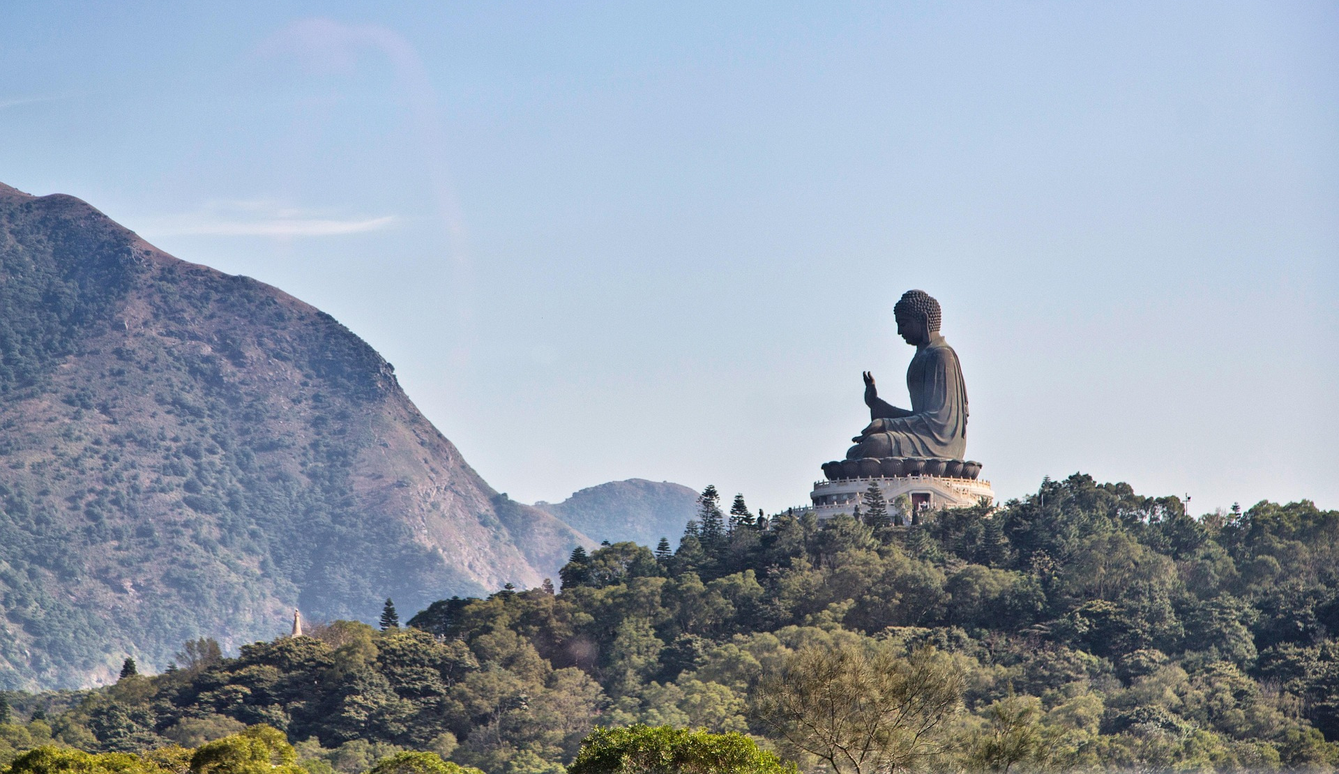 Monumentaler Tian Tan Buddha (Big Buddha) auf Lantau Island, Hongkong, thronend auf grünem Hügel mit Berglandschaft im Hintergrund