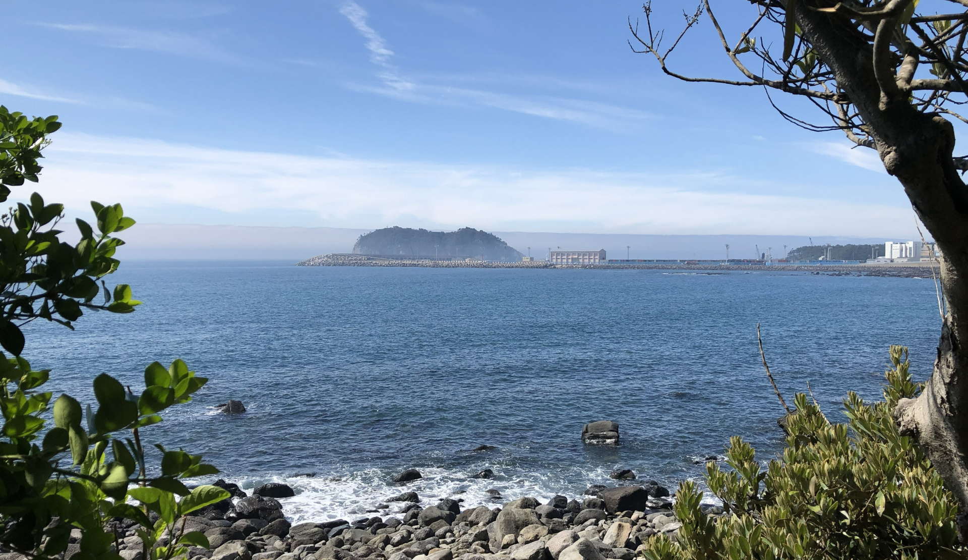 Felsige Küste auf Jeju Island mit Blick aufs Meer und eine kleine Insel im Hintergrund