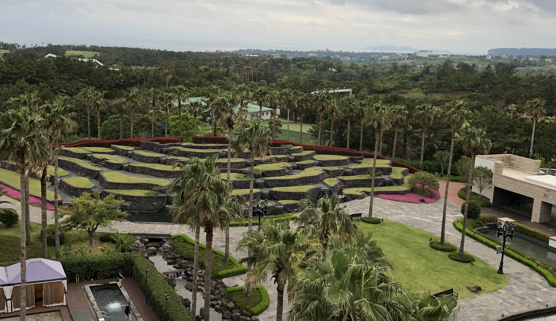 Blick von der Dachterrasse des Kensington Jeju Hotels auf die Gartenanlage mit Palmen und dem Hallasan im Hintergrund