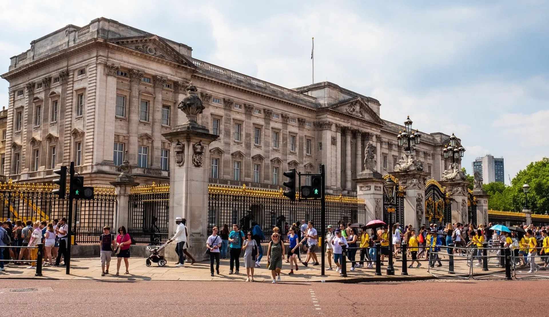 Die Fassade des Buckingham Palace in London hinter schwarz-goldenen Zäunen, davor viele Besucher auf dem Gehweg