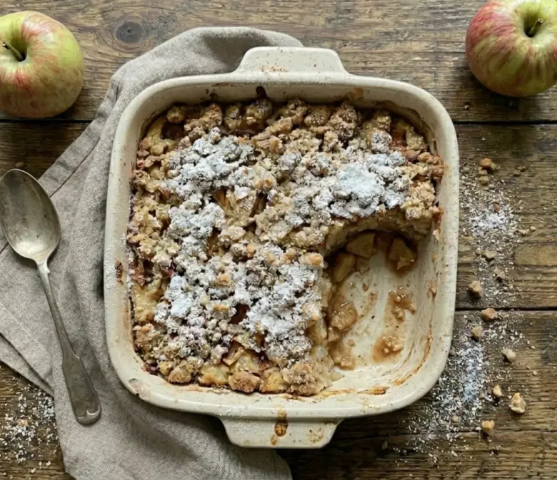 Milchreisauflauf mit Äpfeln und Streuseln in einer Auflaufform, mit einem Stück bereits entnommen