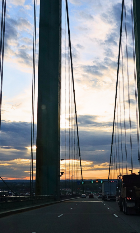 Roadtrip USA über eine Hängebrücke bei Sonnenuntergang, Seile und Pylon im Gegenlicht