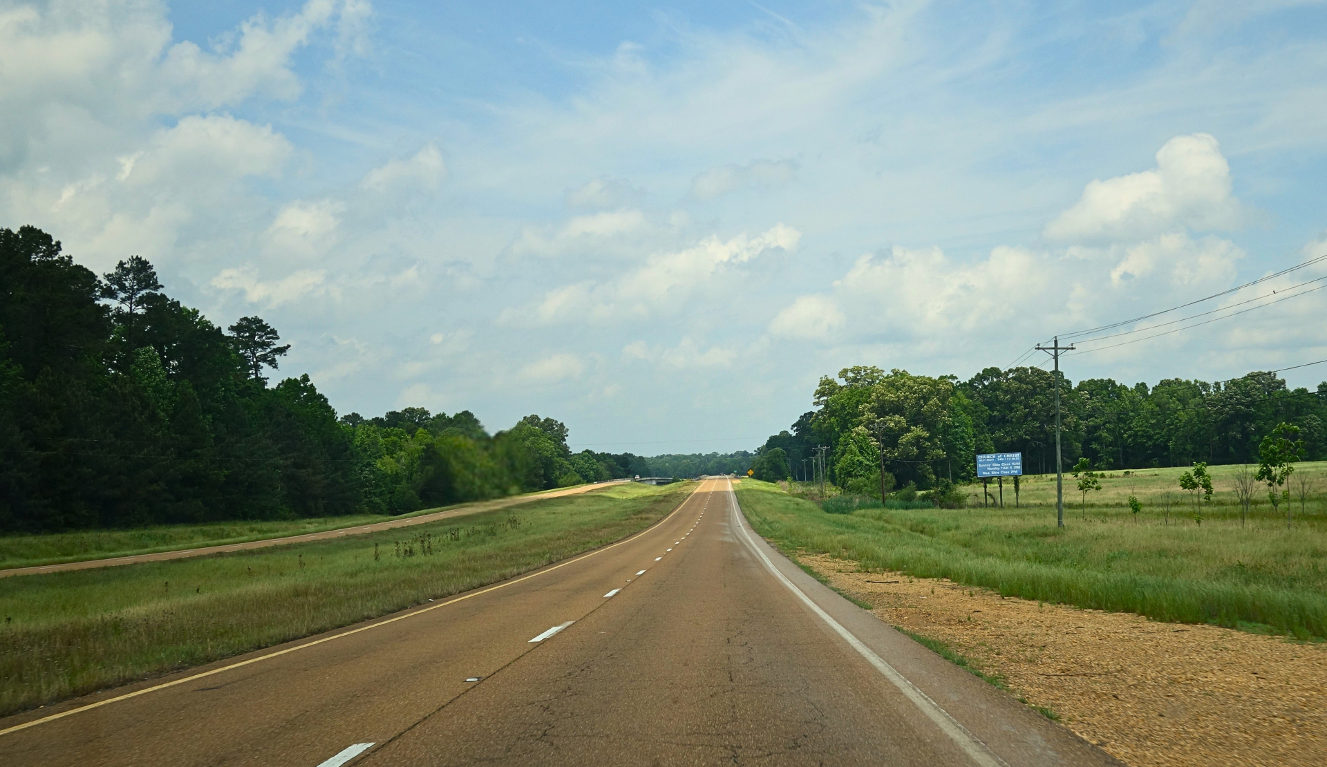 Roadtrip USA: endlose Landstraße im Süden mit Wald und blauem Himmel