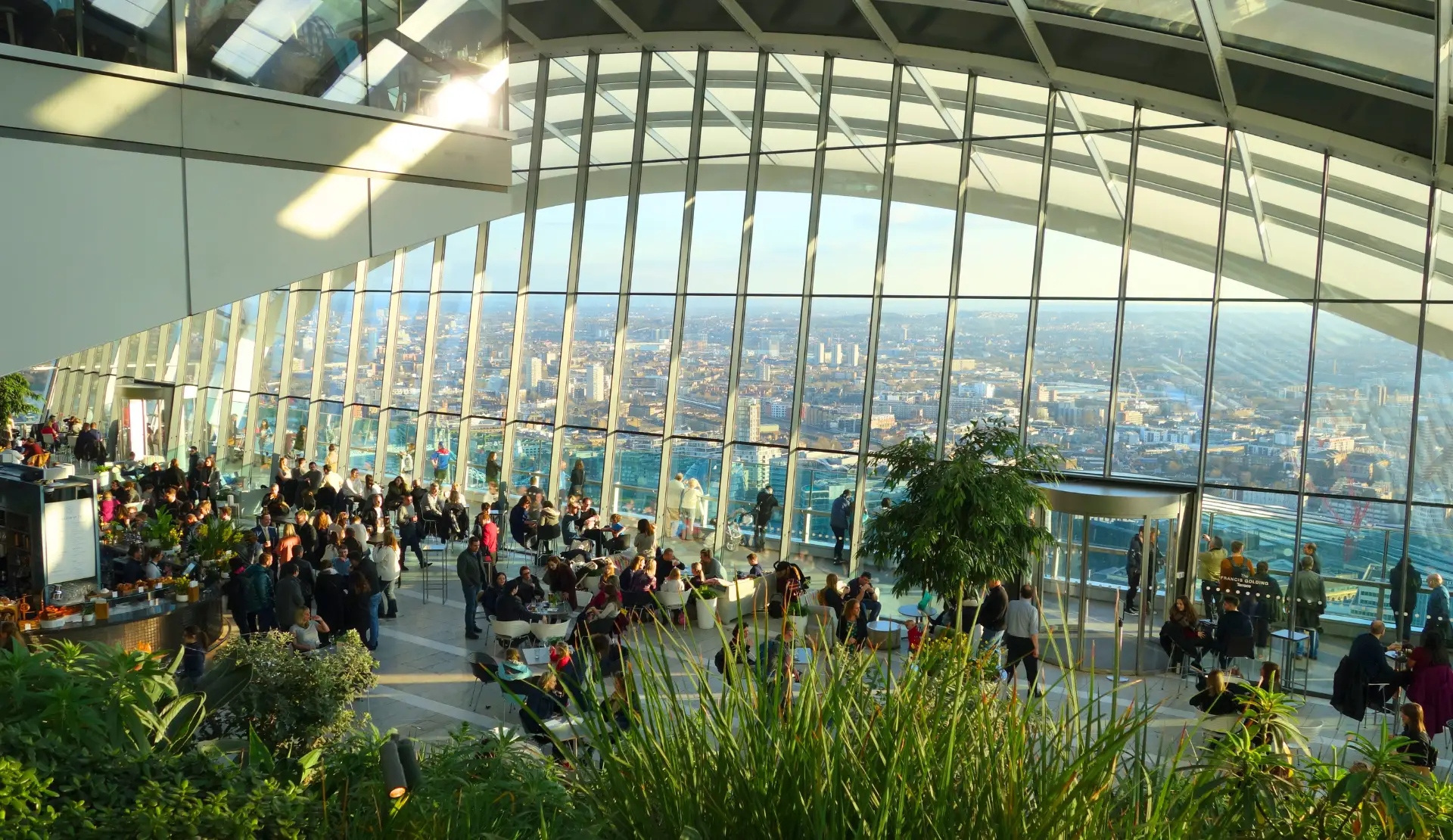 Blick durch die Glaskuppel des Sky Garden London auf Besucher zwischen Pflanzen mit Skyline im Hintergrund