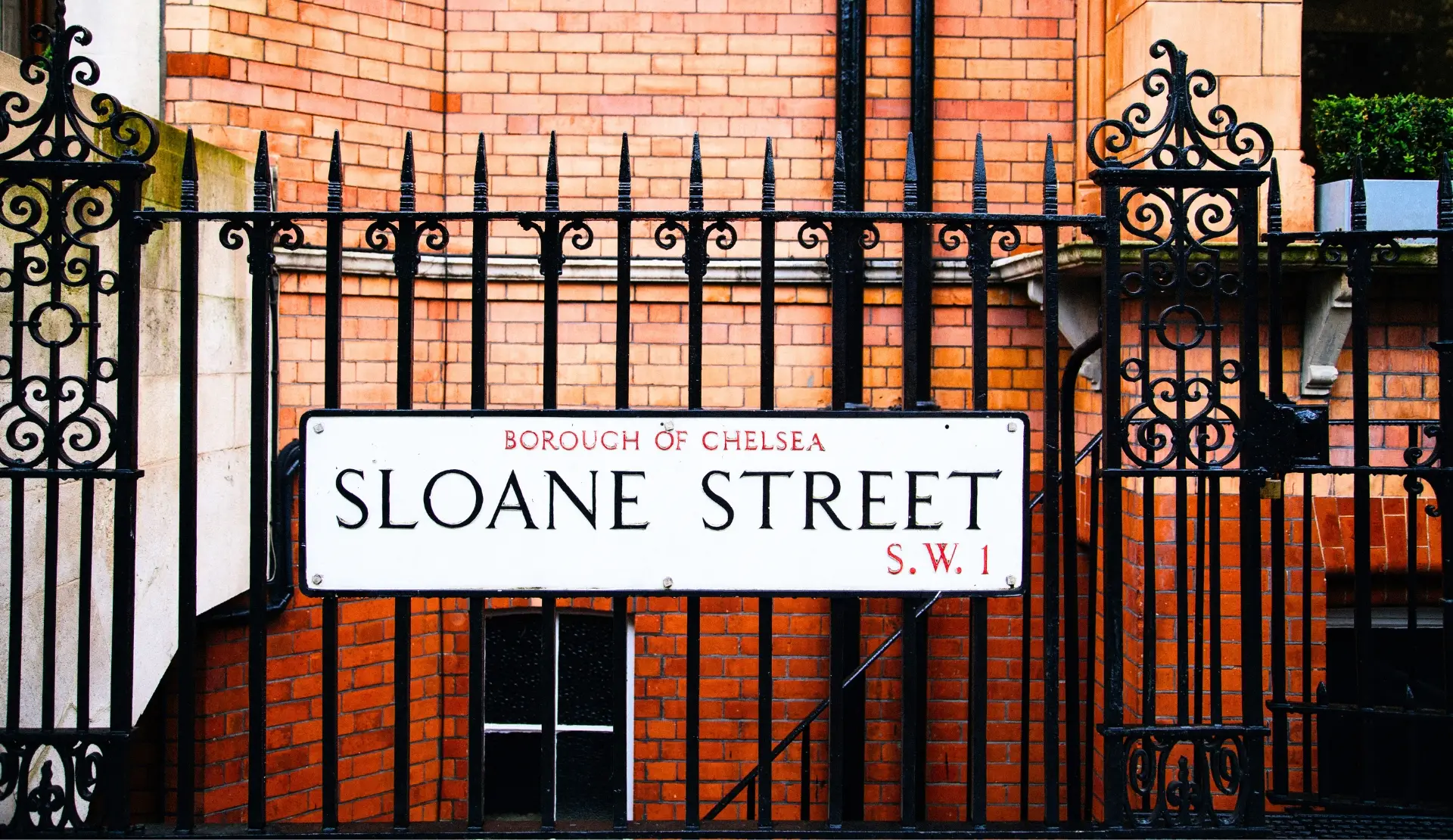 Schmiedeeisernes Tor und Straßenschild Sloane Street im eleganten Stadtteil Chelsea in London.
