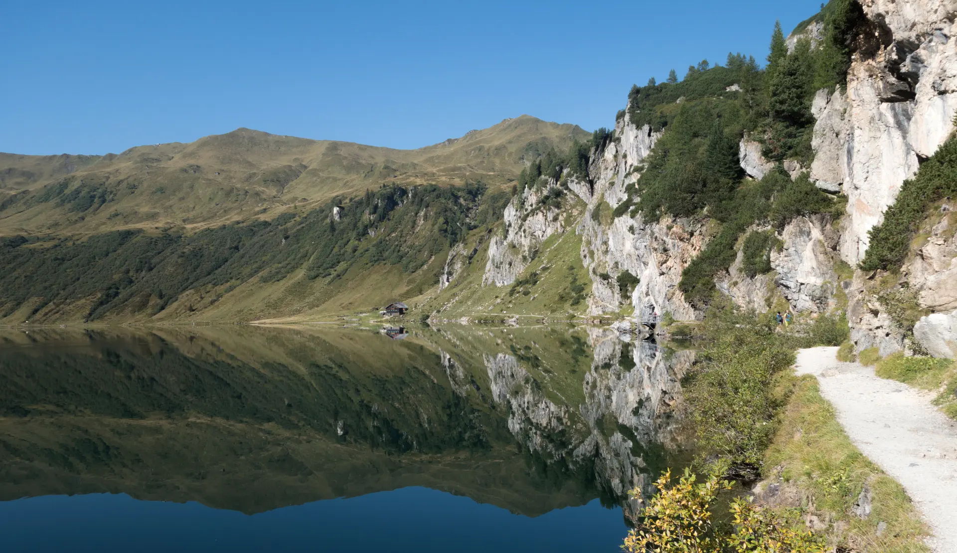 Tappenkarsee mit Spiegelung der grünen Berghänge, Felswand und hellem Uferweg