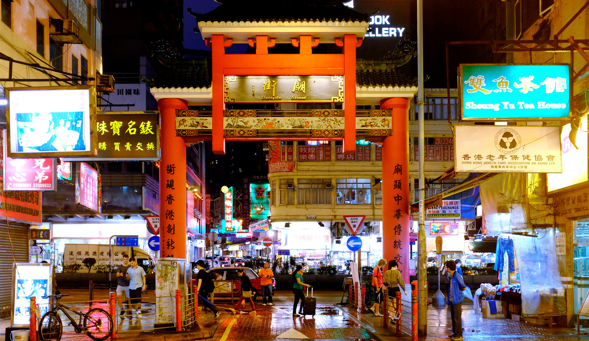 Temple Street Night Market in Hongkong mit leuchtenden Neonreklamen, traditionellem rotem Pailou-Torbogen und geschäftiger Straßenszene bei Nacht