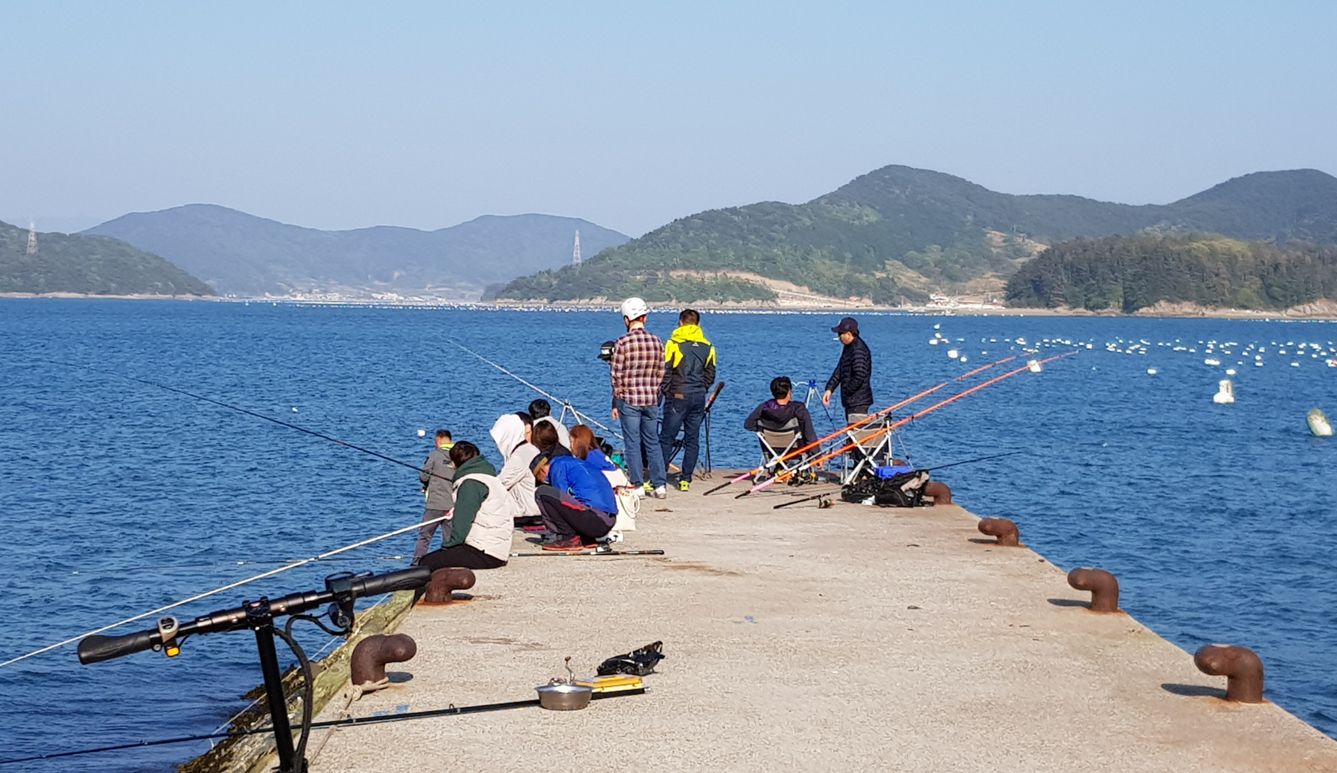 Angler auf dem Steg in Tongyeong mit Blick auf das Meer und die umliegenden Berge, Südkorea