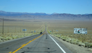 Endlose gerade Highway-Straße durch die Wüstenlandschaft von Nevada mit Bergkette im Hintergrund