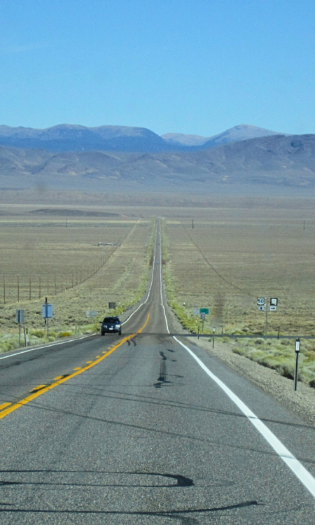 Endlose gerade Highway-Straße durch die Wüstenlandschaft von Nevada mit Bergkette im Hintergrund
