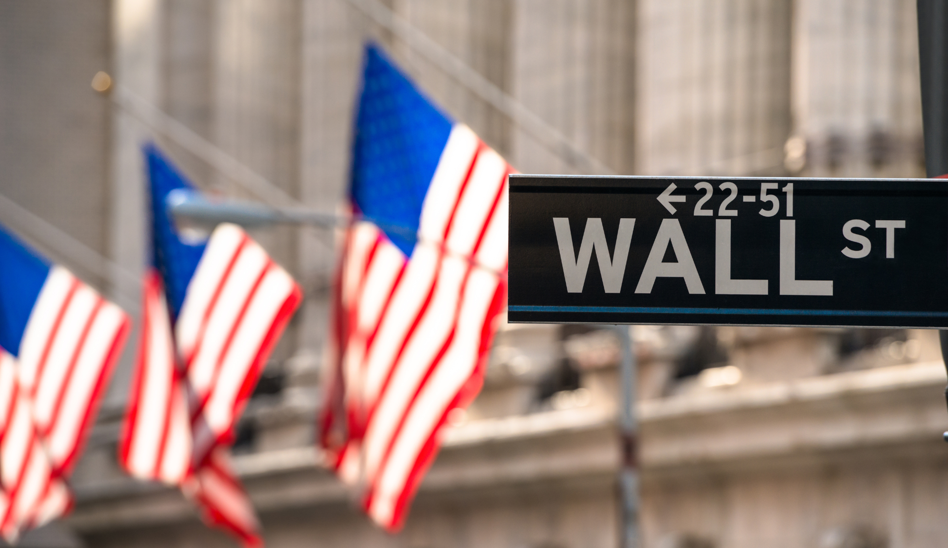 Wall Street Straßenschild mit US-Flaggen im Hintergrund im Finanzdistrikt von New York City